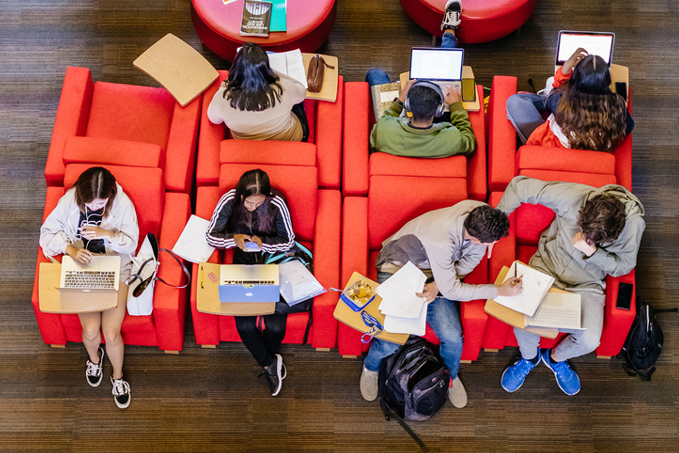 Overhead photo of individuals sitting on red chairs on various devices